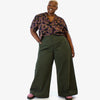 Person wearing a patterned top and green wide-leg pants on a white background