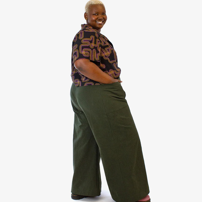 Person wearing a patterned shirt and green wide-leg pants on a white background