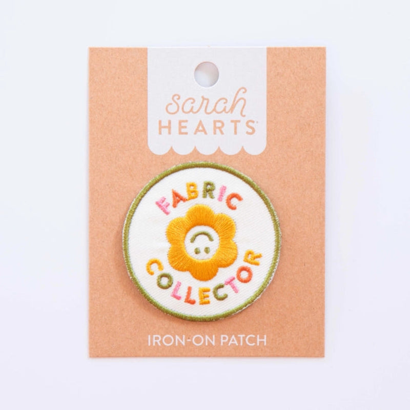 An iron-on patch featuring a smiling yellow flower with the words "Fabric Collector" in colorful letters on Sarah Hearts backing. 