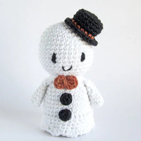 A white crocheted snowman toy with a black top hat, black buttons, and an orange-brown bow tie, photographed against a plain white background.