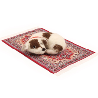 A small brown and white felted puppy toy wearing a red collar, curled up asleep on a miniature red patterned rug against a plain white background.