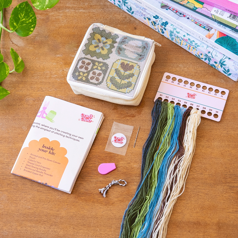 the kit for square zippered pouch with a classic floral needlepoint design, with all the materials displayed on a table