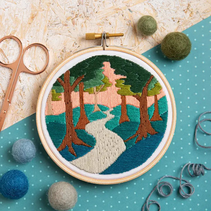 Embroidery hoop with a nature-themed design on a polka dot background with embroidery tools.