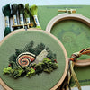 Embroidery hoop with snail design and green thread on a green background