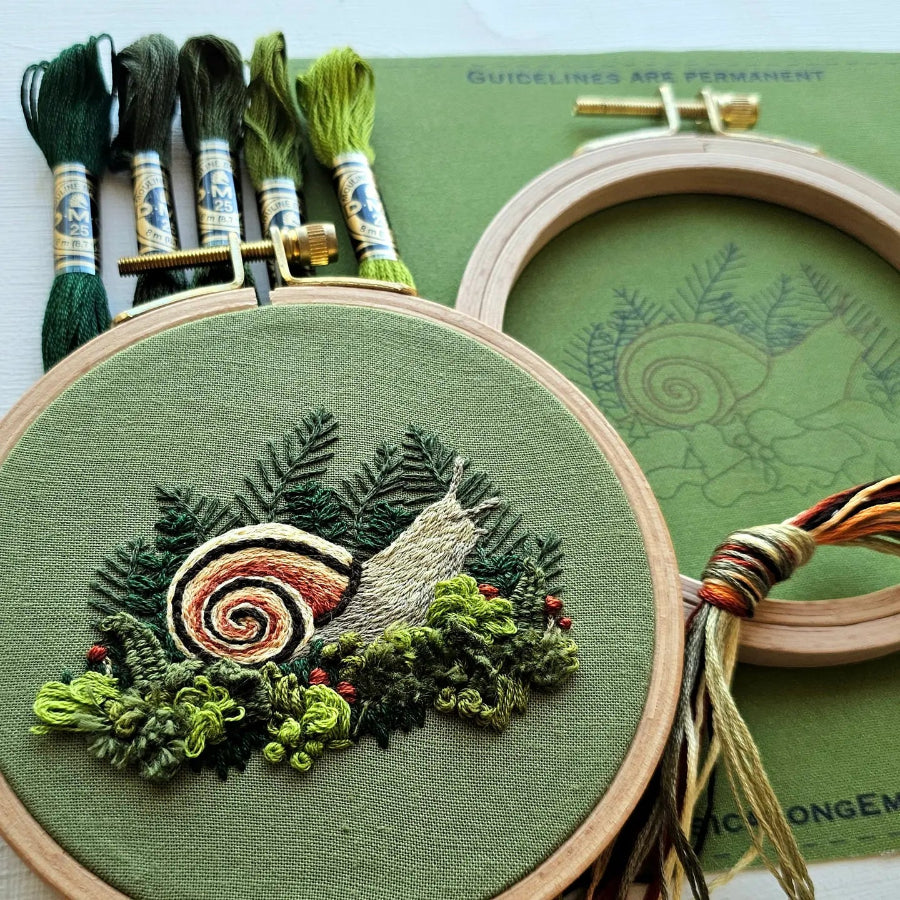 Embroidery hoop with snail design and green thread on a green background