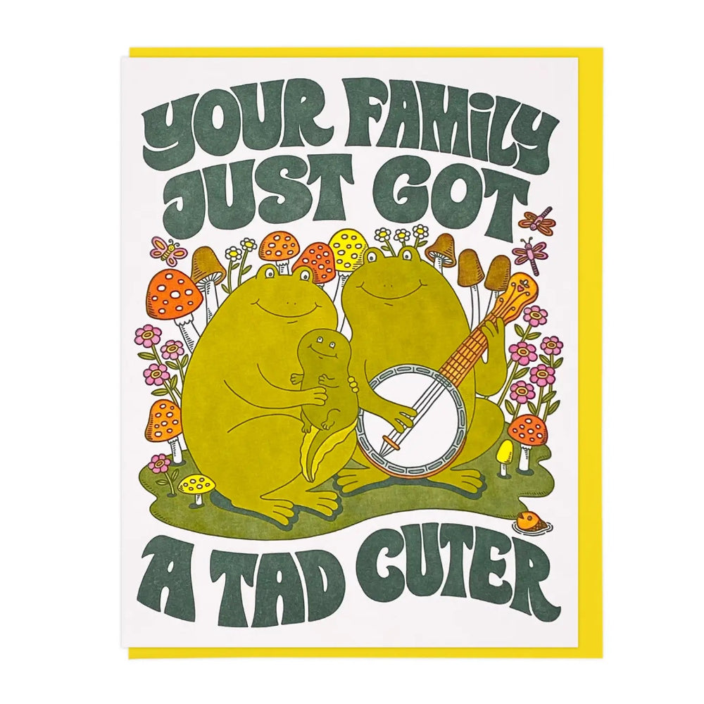 Card with a frog playing banjos next to a frog holding a tadpole. The text reads 'Your family just got a tad cuter' on a white background.