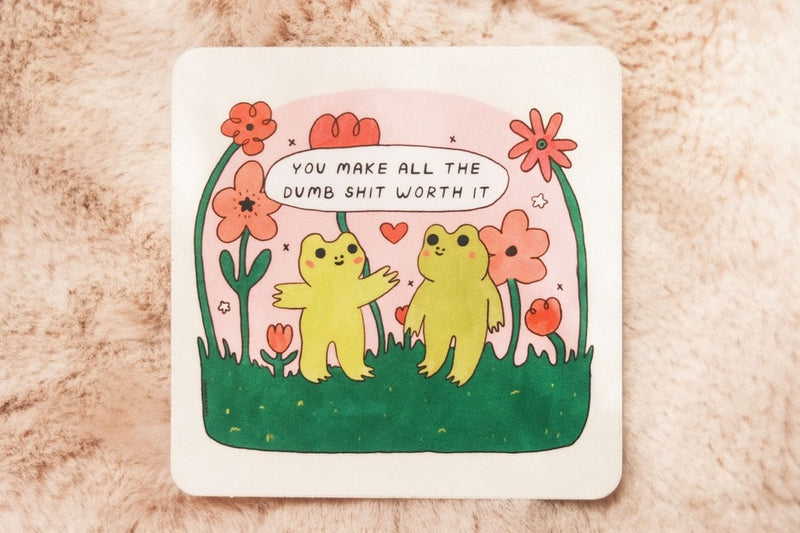 Two frogs standing amidst flowers and grass with one frog saying "You make all the dumb shit worth it".