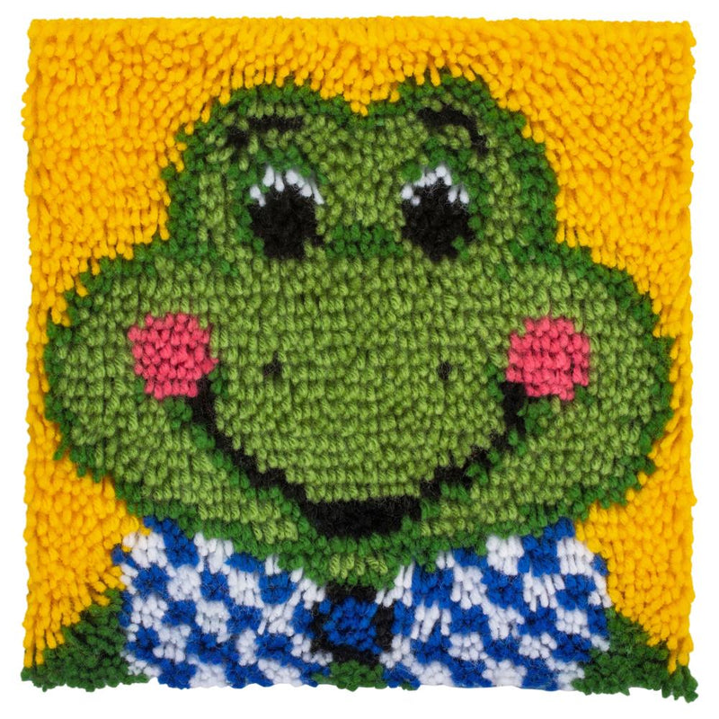 Completed latch hook square project, featuring a cartoon froggy design on a yellow background. The froggy has rosy cheeks and is wearing a blue and white checkered vest.