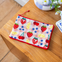 A rectangular zipper pouch decorated with needlepoint images of colorful fruits on a pink checked background