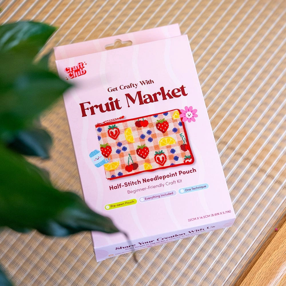A package with the text 'Fruit Market', showing a rectangular zipper pouch decorated with needlepoint images of colorful fruits on a pink checked background