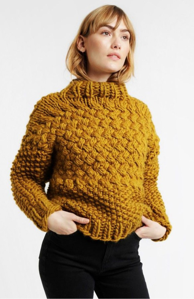 Woman in thick textured knit sweater and black jeans on a white background.