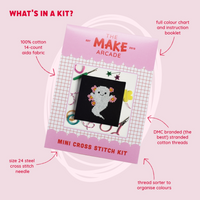 A square black cross-stitch canvas featuring a white ghost design  packaged in pink with the title "The Make Arcade: Mini Cross Stitch Kit", with features about the kit listed around packaging.