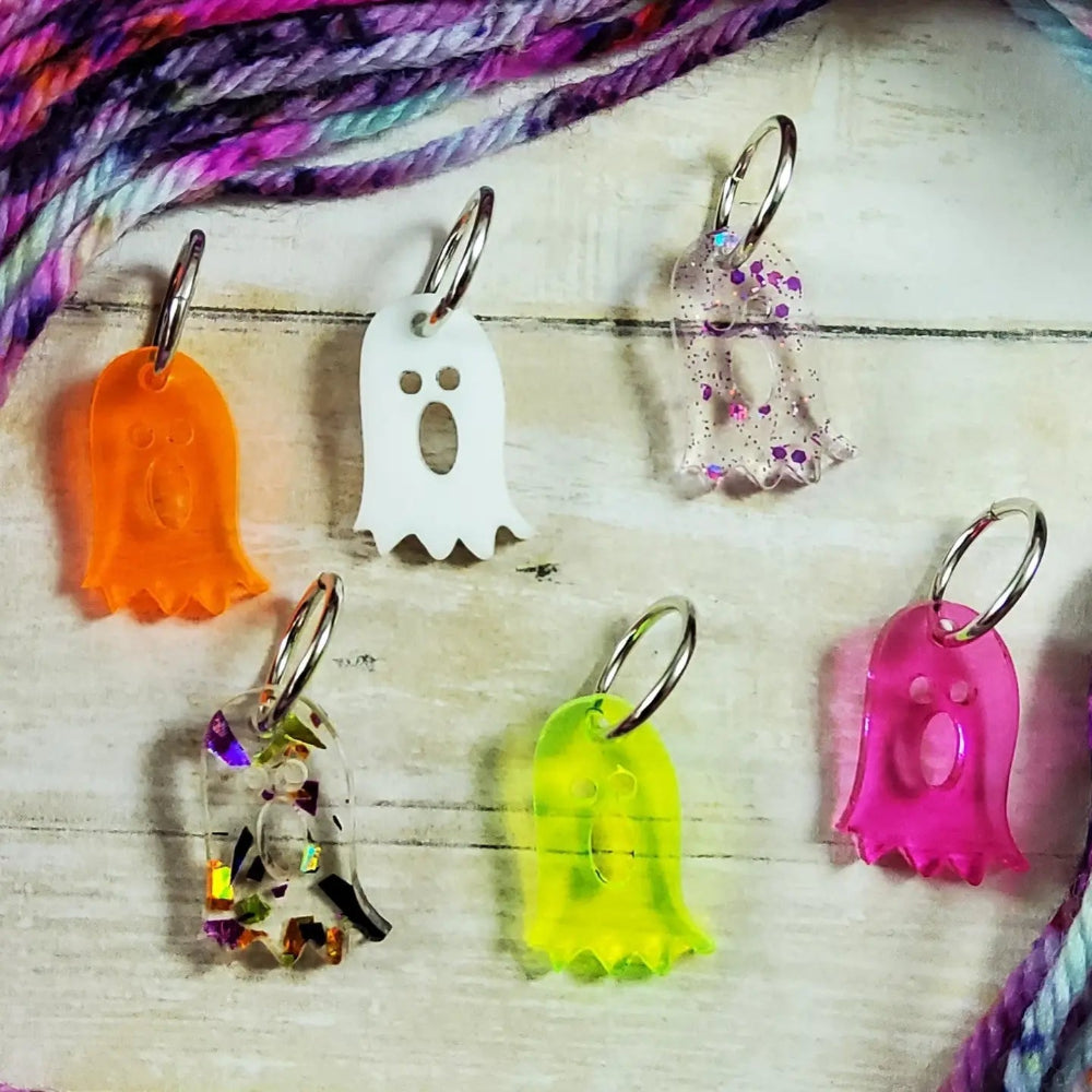 Six cute ghost stitch markers with bright colors and steel rings sit on a wood table
