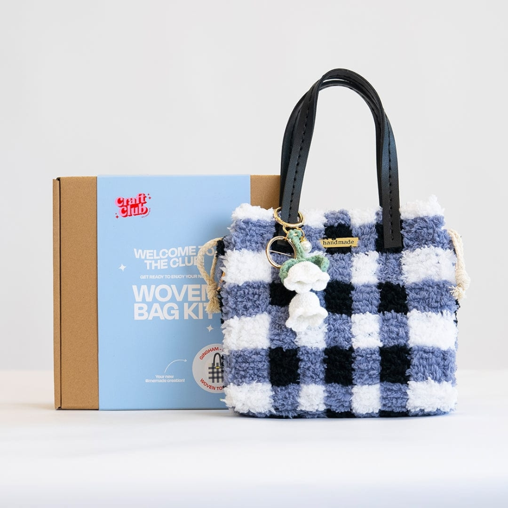 A fluffy blue checkered purse with a floral keychain rests against a box with the label "Woven Bag Kit".