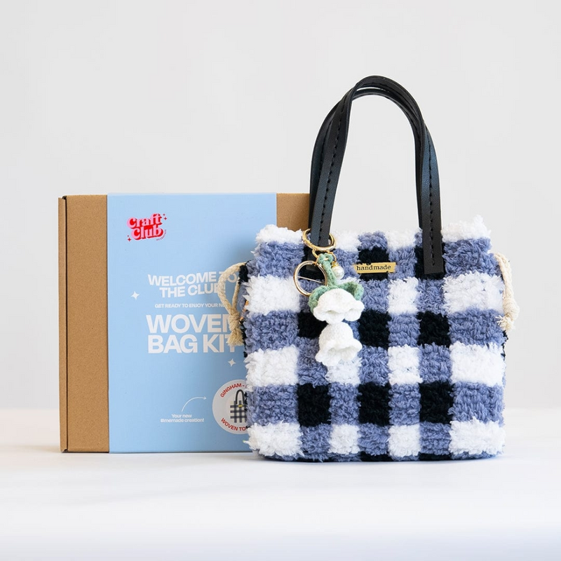 A fluffy blue checkered purse with a floral keychain rests against a box with the label "Woven Bag Kit".