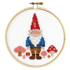 Cross-stitched gnome with red hat and mushrooms in a wooden hoop on a white background