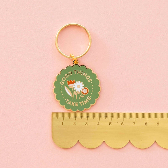 Keychain with floral design and 'Good things take time' text on a pink background with a ruler for scale.