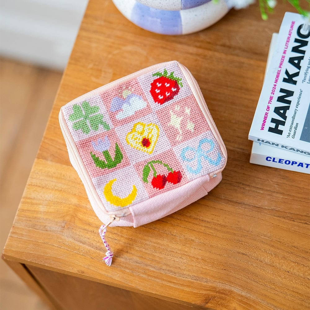 A square zipper pouch with a needlepoint design featuring flowers, clover, a moon and more cute pictures