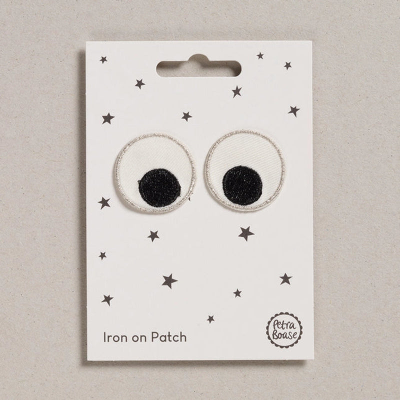 Pair of round eye iron-on patches with black centers on a white card with star patterns, branded 'Petit Bateau'.