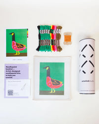 Needlepoint kit materials including a canvas, thread, and instructions on a white background