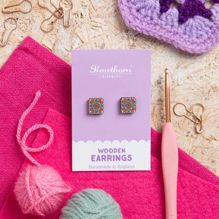 Wooden earrings in a box with yarn and crochet hook on a textured surface