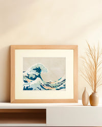 Framed needlepoint artwork with a wave design resting on a white shelf against a tan background