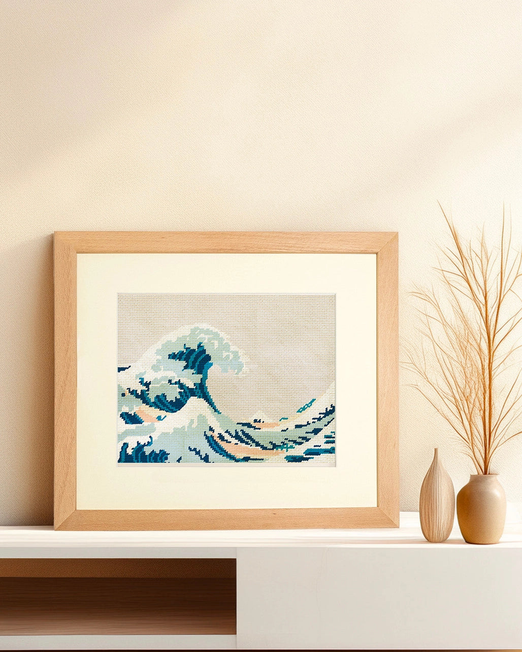 Framed needlepoint artwork with a wave design resting on a white shelf against a tan background