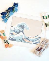 Needlepoint canvas with a wave design surrounded by skeins of thread in various colors