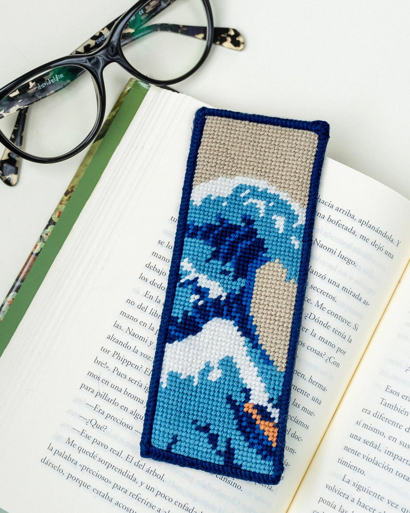 Needlepoint bookmark with a wave design on an open book with glasses on a white background