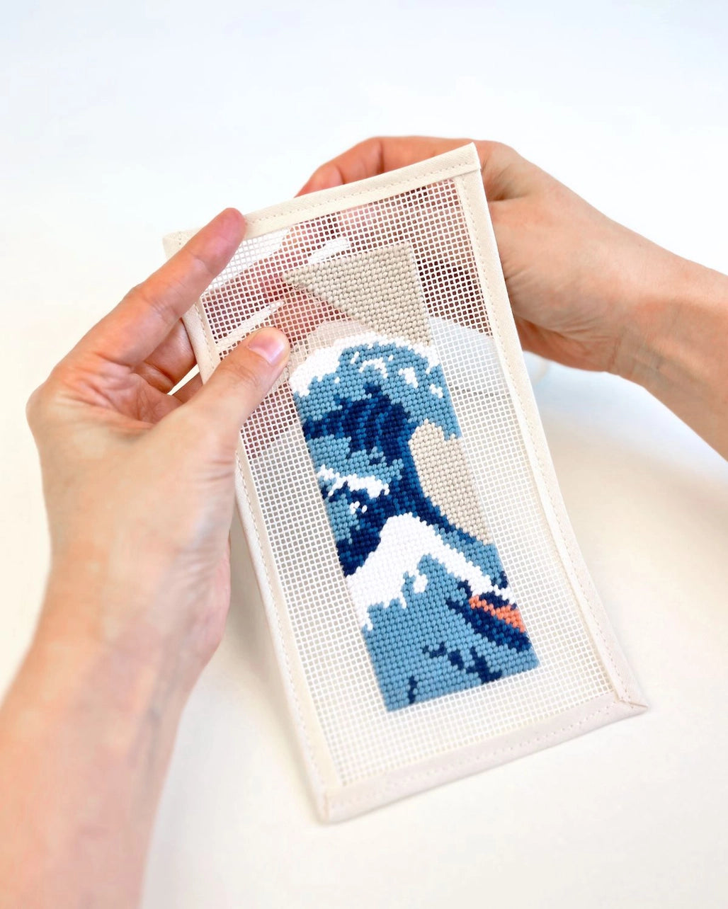 Hands holding a needlepoint bookmark with a wave design on a white background