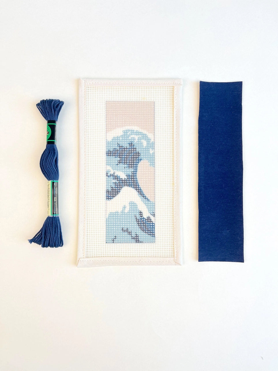 A skein of blue thread, a needlepoint canvas, and a piece of blue felt on a white background