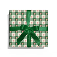 Gift box with green checkered pattern and pink dots, tied with a green ribbon on a white background