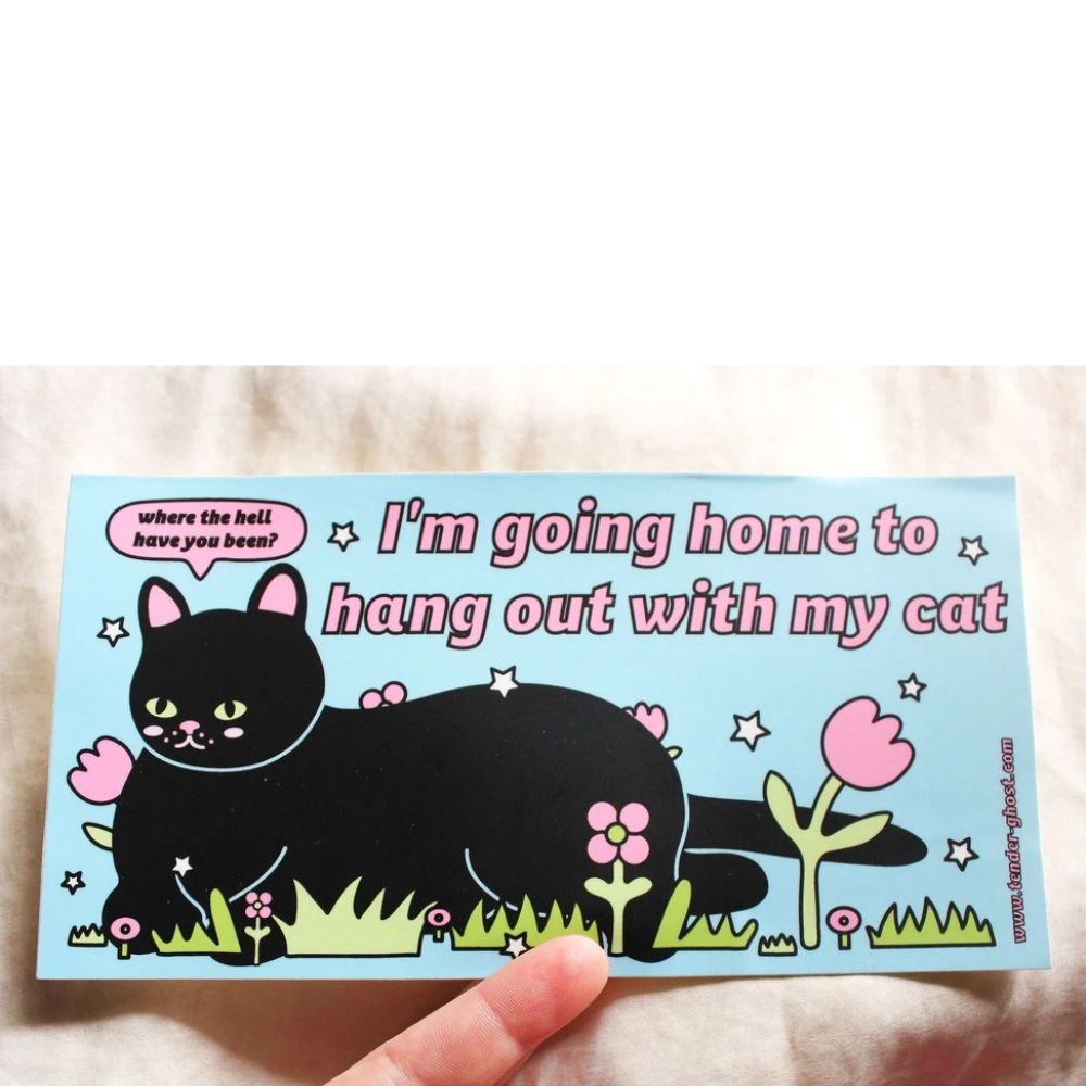 Sticker with a black cat illustration and text on a light blue background, held by a hand.