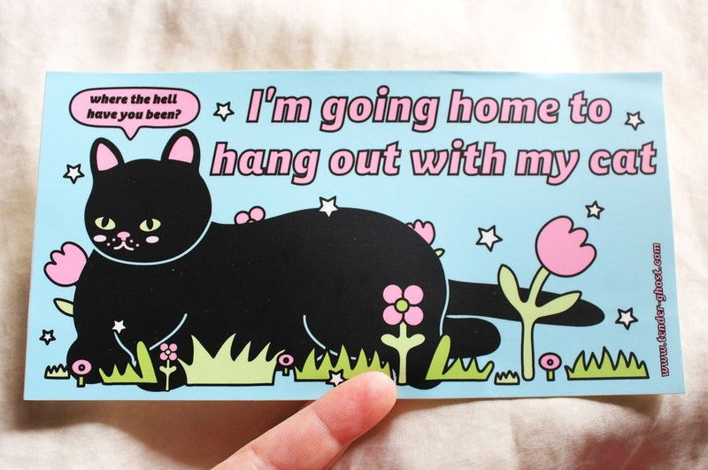 Black cat laying in grass and flowers with a blue background and the words "I'm going home to hang out with my cat". The cat's speech bubble says "Where the hell have you been?".