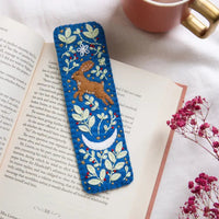 Embroidered bookmark with a hare design on an open book next to a cup and flowers.