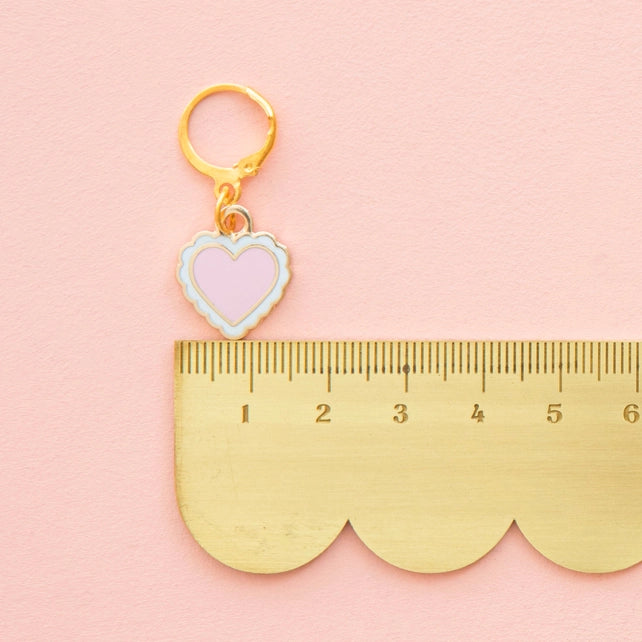 Heart-shaped stitch marker on a pink background