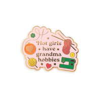 Enamel pin with text 'Hot girls have grandma hobbies' and various sewing-related icons on a white background.