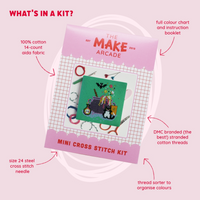 A square green cross-stitch canvas featuring a purple cauldron and various Halloween elements, packaged in pink with the title "The Make Arcade: Mini Cross Stitch Kit", with features about the kit listed around packaging.
