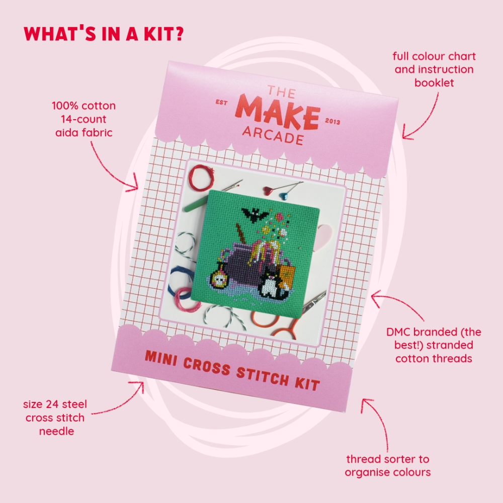 A square green cross-stitch canvas featuring a purple cauldron and various Halloween elements, packaged in pink with the title "The Make Arcade: Mini Cross Stitch Kit", with features about the kit listed around packaging.