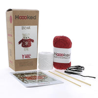A photo of the box and contents of the Bear Yule Crochet Kit Kit from Hoooked, including red and white yarn, two crochet ooks and an instruction booklet.