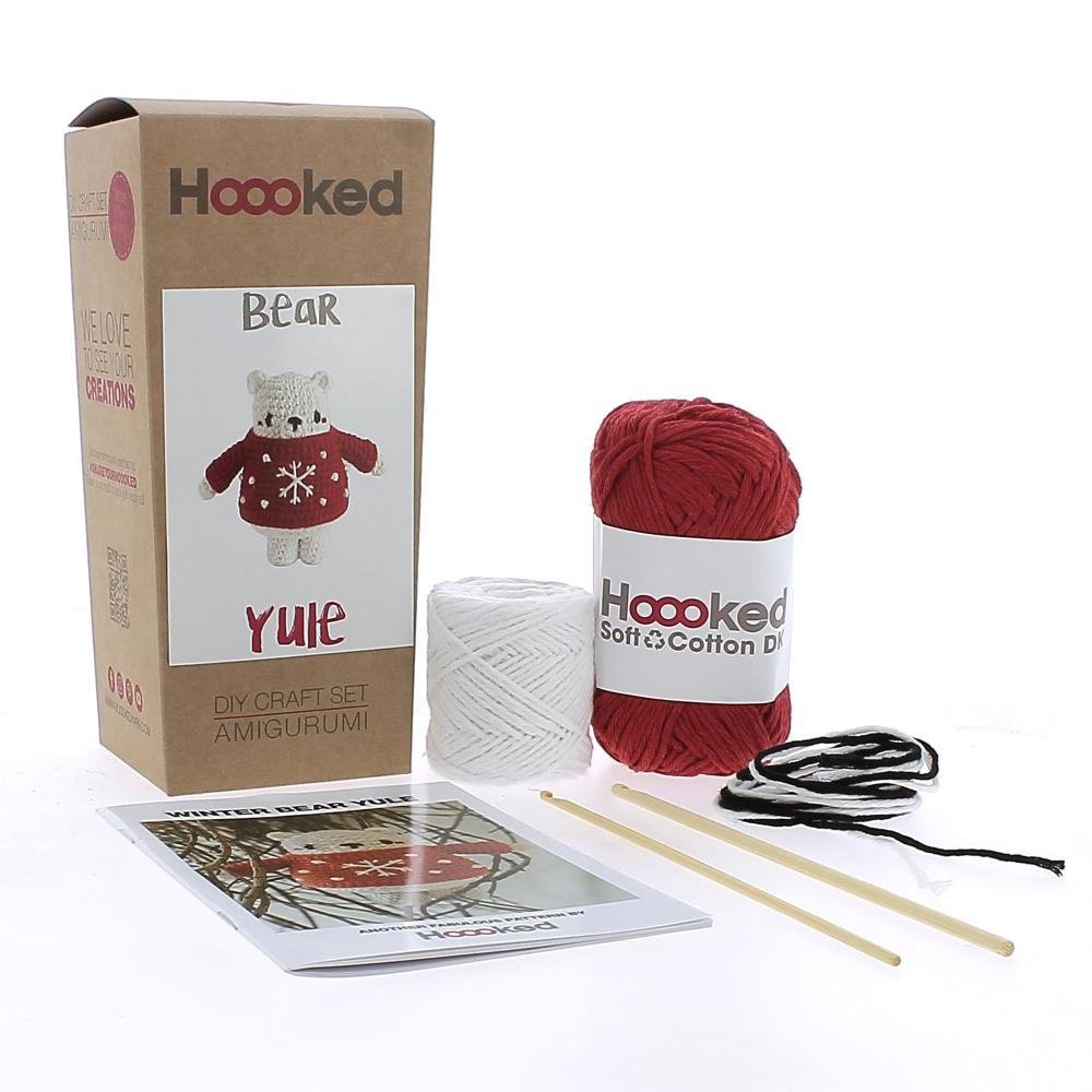 A photo of the box and contents of the Bear Yule Crochet Kit Kit from Hoooked, including red and white yarn, two crochet ooks and an instruction booklet.
