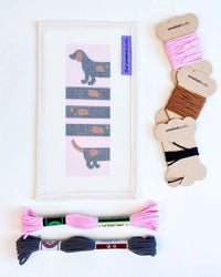 Needlepoint kit with dog design, skeins and bobbins of thread against a white background