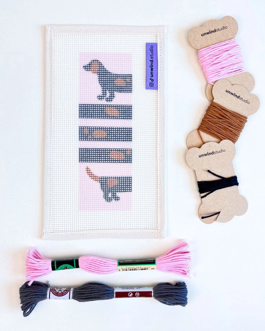 Needlepoint kit with dog design, skeins and bobbins of thread against a white background