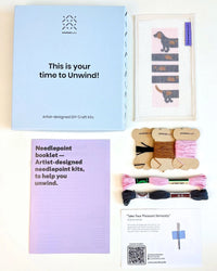 Craft kit with needlepoint canvas and thread, featuring 'Unwind Studio' branding.