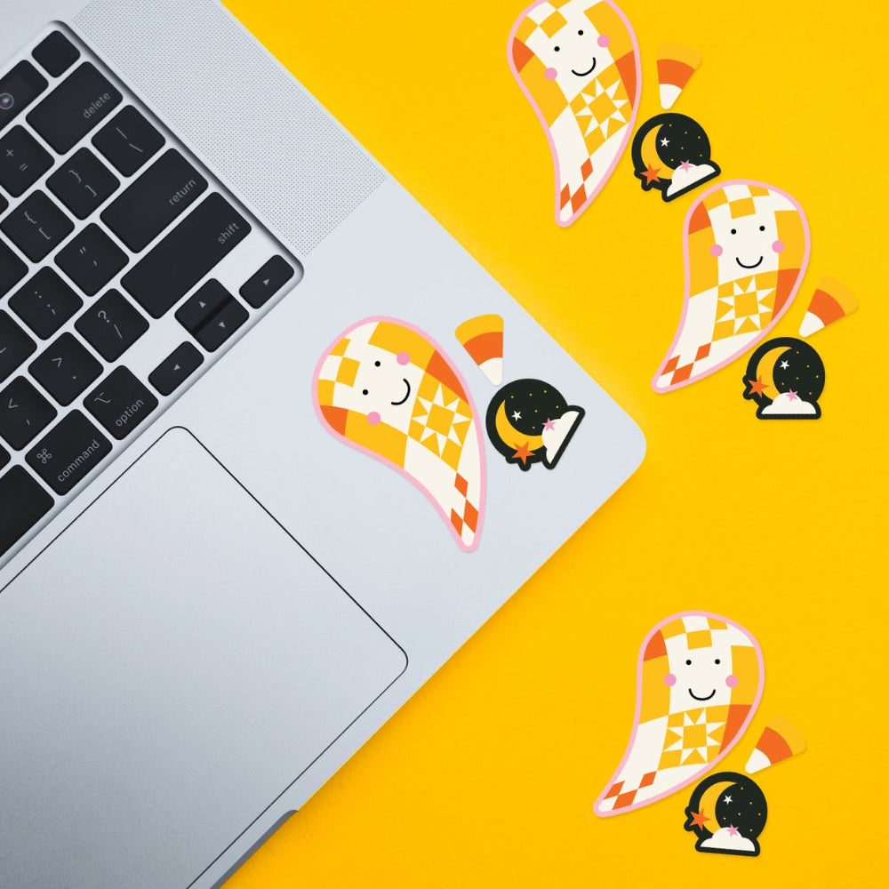 A sticker set featuring a cute ghost character with a checkered yellow and orange pattern, a crescent moon, and a book. The sticker is shown applied to a silver laptop on a bright yellow surface, with additional duplicate stickers scattered on the right side.