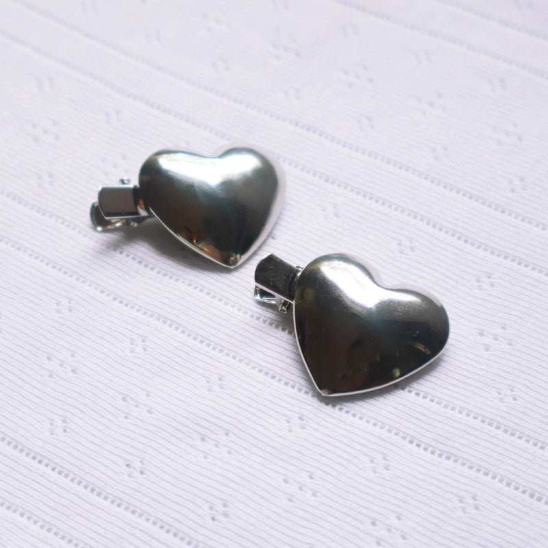 Silver heart-shaped hair clips on a textured white background