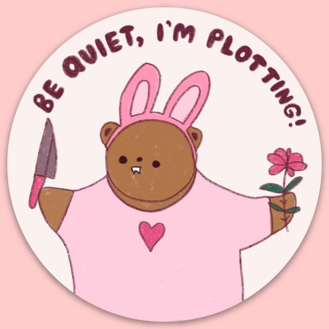 Bear dressed with bunny ears and pink shirt while holding a flower and trowel with the words "Be quiet, I'm plotting!".