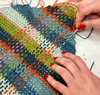 Hands weaving yarn into a mesh crochet panel. 