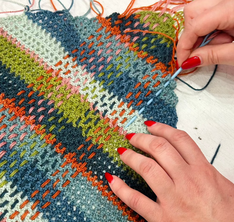 Hands weaving yarn into a mesh crochet panel. 