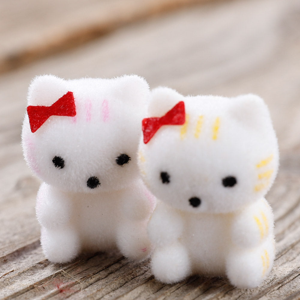 Two miniature flocked kittens with red bows sit on a wood surface. One has yellow stripes and one has pink stripes.